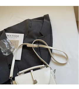 Top-down view of a white vintage faux leather crossbody bag on a grey suit with metal buckle