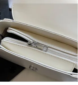 Detail view of smooth silver metal zipper and interior magnetic buckle on white crossbody bag