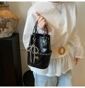 Detail einer schwarzen gesteppten Beuteltasche mit Kette und Perlen-Schleife
