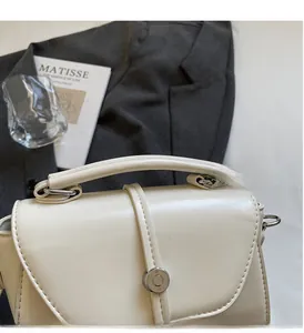 Detail of a creamy white leather handbag with a circular metal buckle and thick top handle