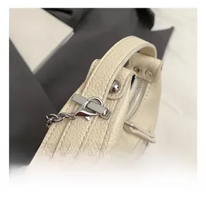 Detail of silver metal hook and cream-colored lychee leather texture on handbag