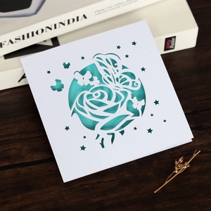 Détail du faire-part de mariage découpé au laser avec rose et papillon sur bois sombre