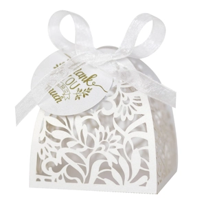 Macro shot of laser-cut white wedding candy box featuring floral details and ribbon