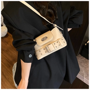 Détail d'un sac seau beige avec œillets argentés et fermoir rotatif sur un blazer noir