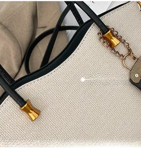 Detail of oatmeal woven tote bag featuring black leather trim and gold metal hardware