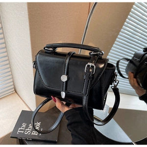 Detail view of glossy black vintage crossbody bag with silver buckle and top handle