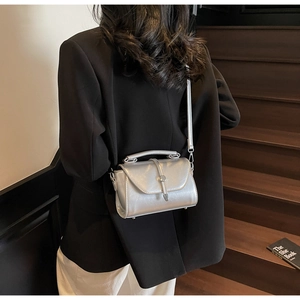 Detail of silver metallic crossbody bag with round magnetic buckle and top handle