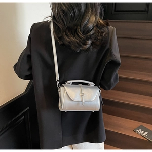 Detail of silver metallic shoulder bag with round clasp shown on model against wooden steps