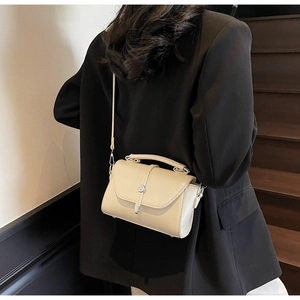 Close-up of cream crossbody square bag with cylindrical metal buckle and slim strap