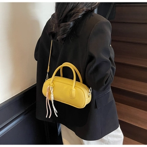 Detail of yellow lychee grain leather pillow bag with pink tassel on wooden stairs