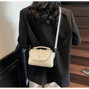 Model wearing a cream square crossbody bag with metal twist lock and top handle