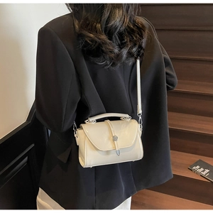 Model wearing a cream white crossbody flap bag with a metal buckle on dark stairs