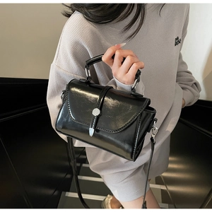 Glossy black patent leather mini bag with silver buckle worn by a model in a studio
