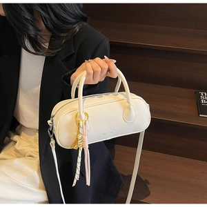 Detailed close-up of a white pebble leather barrel bag with a colorful tassel on wooden steps