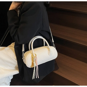 Close-up of white litchi pattern leather pillow bag with braided cord charm on wooden stairs
