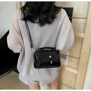 Detailed view of a black crossbody bag with white stitching and silver metal buckle