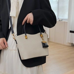 Detail of canvas tote bag featuring black leather handles and gold metal hardware