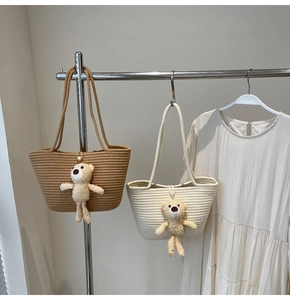 Detail of woven straw tote bag featuring a cute plush bear charm and elegant pearl button