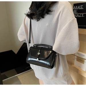 Close-up of a model carrying a glossy black leather shoulder bag with metallic buckle