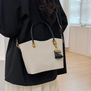 Detail shot of beige tote bag with black handles on shoulder of model in black blazer