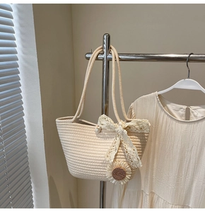 Detail of summer straw tote bag with sunflower pendant and elegant beige lace bow