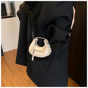 Close-up of beige lychee texture leather bag with silver chain on black blazer background