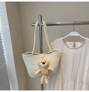 Detail of off-white straw tote bag with pearl buckle and cute plush bear charm decoration