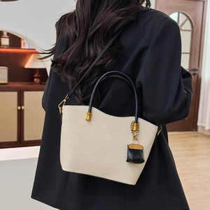 Close-up of woven tote bag with black strap and mini purse charm in home setting