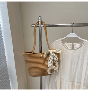 Detail of straw woven tote bag featuring a white lace bow and sunflower charm accessory