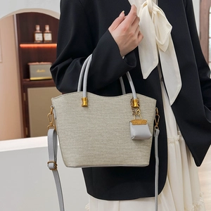 Close-up of woven oatmeal tote bag with gold hardware on a model in a black blazer