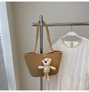 Detail of straw woven tote bag featuring a pearl clasp and cute plush bear charm