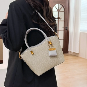 Detail of woven tote bag with gray leather handles and mini bag pendant accessory