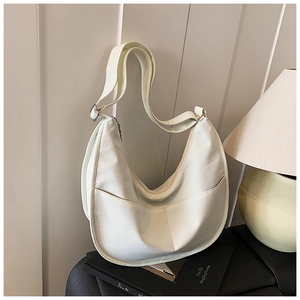 Close-up of a white leather half-moon crossbody bag with symmetrical front pockets and zipper