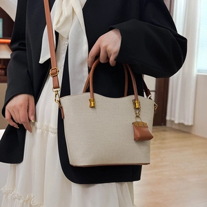 Detail of beige woven tote bag with brown leather handles and a mini bag charm
