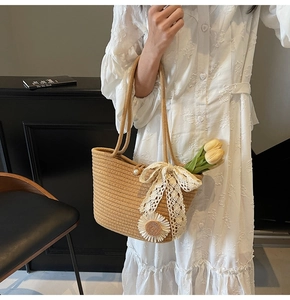 Detail of hand-woven straw tote bag with lace bow, floral charms, and pearl button clasp