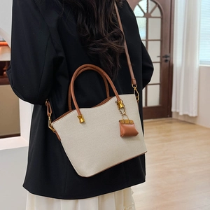 Detail of a beige canvas tote bag with brown leather straps shown on a model