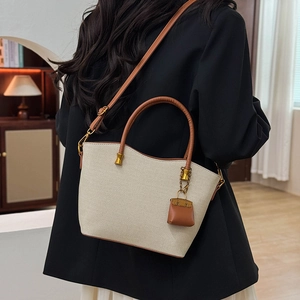 Detail of woven texture canvas tote with brown leather straps and mini bag charm