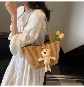 Detail of straw woven tote bag featuring a cute plush bear and elegant pearl clasp closure