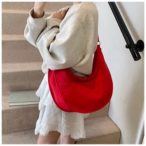 Detailed view of red crescent canvas crossbody bag styled on outdoor stone stairs