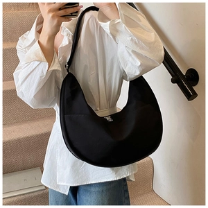 Detail of a black hobo shoulder bag featuring a silver logo and wide strap on model