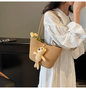 Detail of straw woven tote bag featuring pearl buckle and cute teddy bear pendant charm