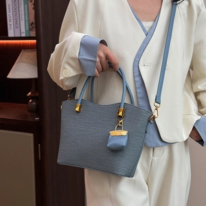 Detail of blue woven tote bag with wavy rim, gold hardware and mini bag charm accessory