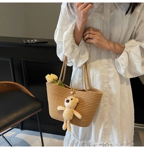 Detail of straw woven tote bag featuring pearl button closure and cute bear pendant charm