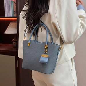 Detail view of a textured grey-blue tote bag with gold metal parts and small coin purse