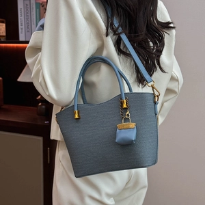Detail of grey-blue tote bag with textured fabric and gold hardware on model