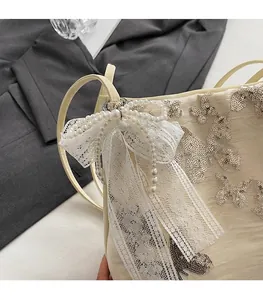 Detail of embroidered sequin butterfly and lace bow with pearls on cream shoulder bag