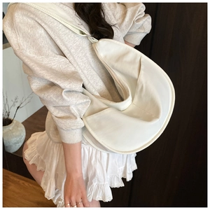 Side view of a white crescent canvas bag worn with a casual outfit in a minimalist setting