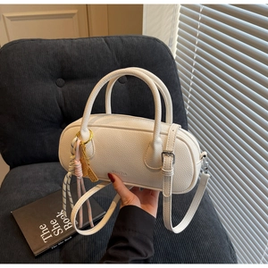 Close-up of white lychee leather cylinder bag with brand logo and woven charm