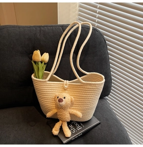 Close-up of straw tote bag with pearl closure and plush bear charm on soft sofa