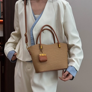 Detail of a brown woven tote bag featuring a mini charm and leather handle for women